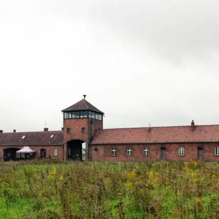 Auschwitz-Birkenau entrance with overcast skies and grass foreground.