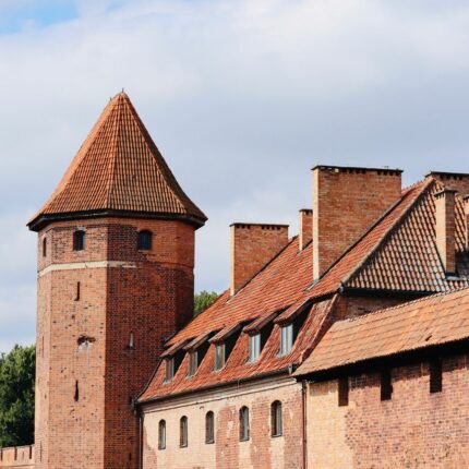 Explore the historic Malbork Castle in Poland, showcasing medieval architecture against a summer sky.