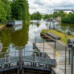 Tranquil canal lock with lush trees and calm waters, perfect for a serene boat trip.